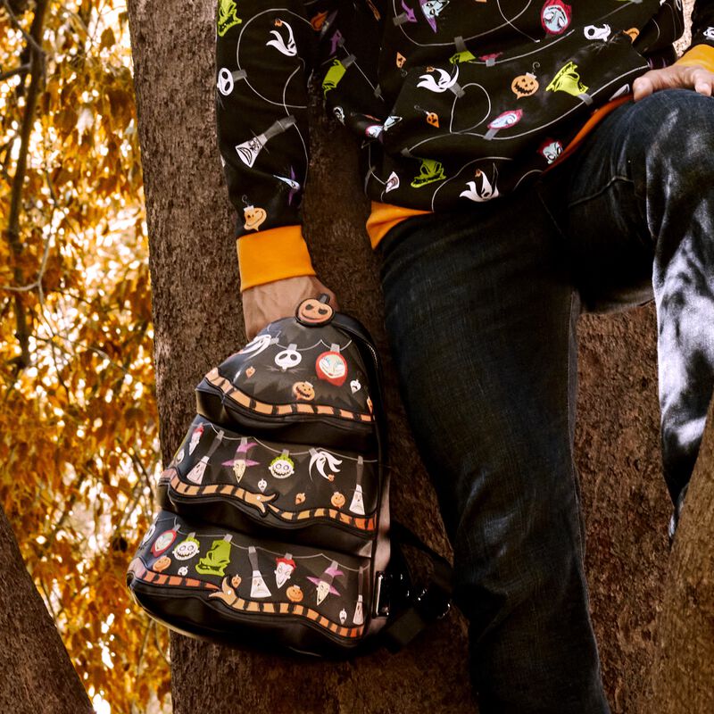 Image of a person leaning against a tree, holding the Nightmare Before Christmas Tree mini backpack in one hand 